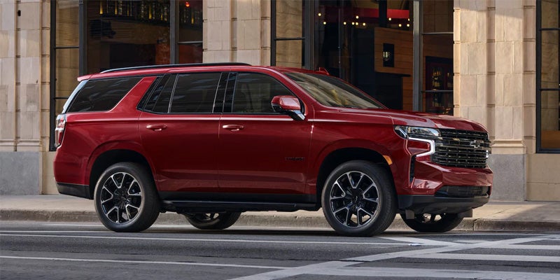 Image of a red 2024 Chevrolet Tahoe driving in-motion down a downtown city street