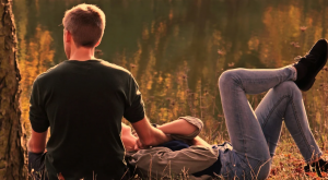 A girl laying on a guy's lap sitting on the ground surrounded by greenery at a park. | St. Louis, MO