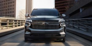 Close view of the front of a charcoal 2021 Chevy Tahoe being driven on the road with buildings in the background. | Chevrolet dealer in St. Louis, MO.
